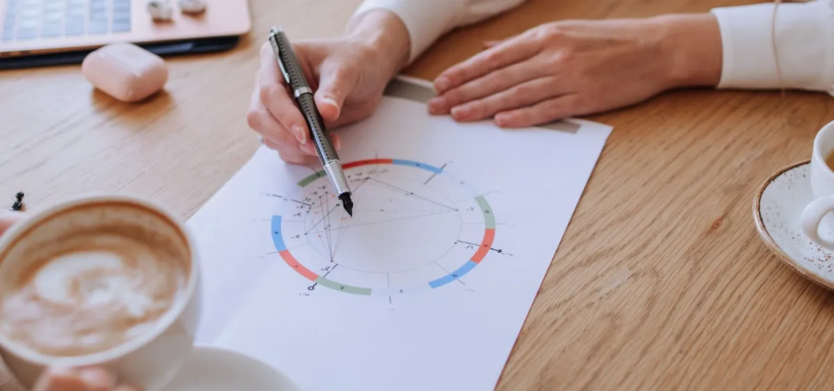 Astróloga analisando um mapa natal impresso sobre a mesa, ao lado de um notebook e uma xícara de café.